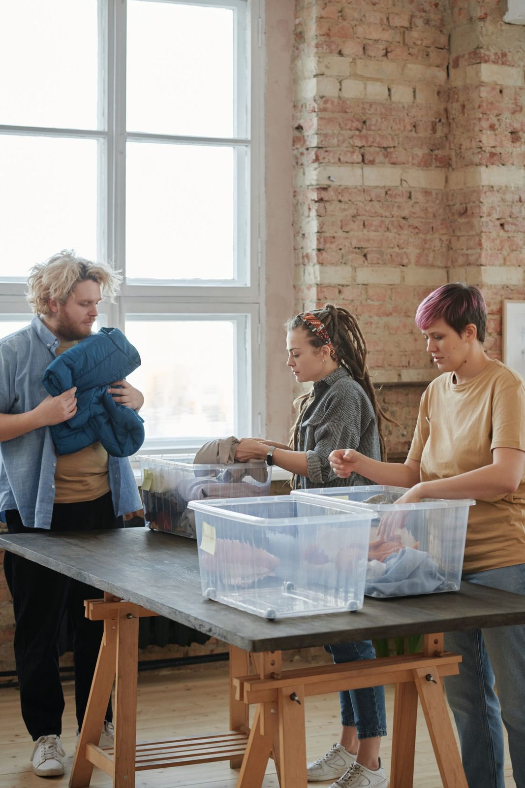 Three volunteers sorting clothes indoors. Engaged in organizing for charity, teamwork, and community service
